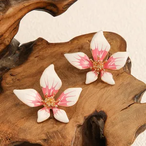 Vista dettagliata di orecchini a fiore a cinque petali in smalto rosa sfumato su legno