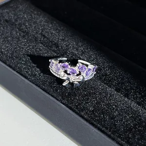 Gros plan d'une bague argentée avec cristaux violets et motif nœud cygne.