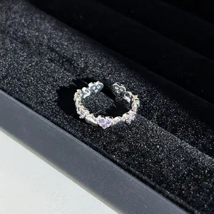 Gros plan d'une bague en argent avec strass en cœur violets dans un écrin en velours.