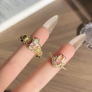 Vista detallada de anillos vintage dorados con flor de lis y piedras rosas en mano