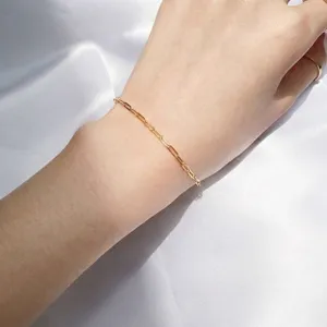 Minimalist 14K gold-filled paperclip link bracelet on wrist against soft white fabric