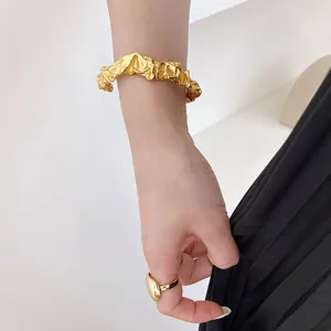 Detailansicht eines goldfarbenen Armreifs mit Textur und passendem Ring an der Hand