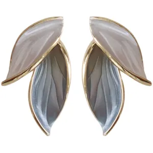 Close-up of minimalist leaf-shaped stud earrings in gold and pearl tones