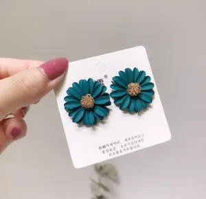 Detail shot of teal daisy flower stud earrings on a white branded display card