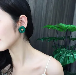Detailed view of green daisy flower stud earrings worn by a model in nature