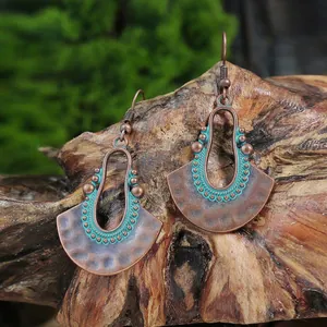 Dettaglio di orecchini bohémien in bronzo con accenti di smalto verde acqua su legno