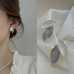 Elegant leaf-shaped earrings in white and grey on a model and silk background