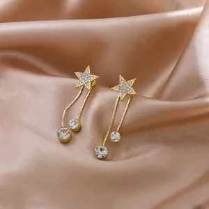 Détail macro exquis de boucles d'oreilles étoiles dorées à pompons et strass brillants sur soie
