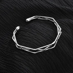 Gros plan d'un bracelet jonc ouvert géométrique argenté sur un tissu noir texturé.