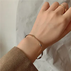 Detailed view of an elegant minimalist wavy gold-toned open bangle and matching ring on model