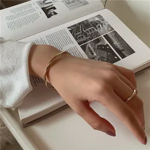 Close-up view of a minimalist golden wave-patterned open bangle and a simple gold ring