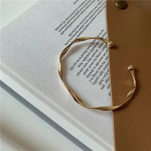 Detailed close-up of a gold wavy twisted open cuff bracelet on a minimalist background