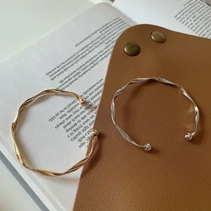 Elegant wavy open bangles in gold and silver finishes displayed on a minimalist background