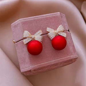 Primo piano di orecchini a fiocco eleganti con perle rosse su scatola rosa.