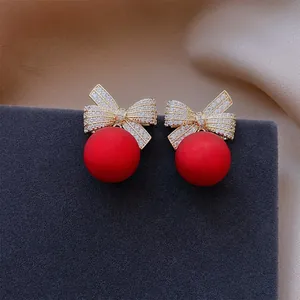Primo piano di orecchini eleganti a fiocco dorati con perle rosse e strass luccicanti.