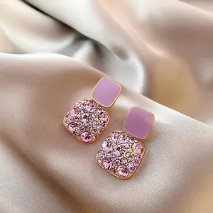 Eleganti orecchini quadrati in oro con cristalli rosa su sfondo di raso champagne