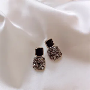 Primo piano di orecchini quadrati eleganti con pietra nera e cristalli grigi su seta.