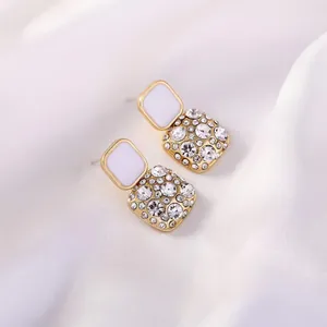 Eleganti orecchini a lobo dorati con smalto bianco e strass scintillanti.