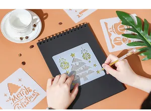 Detailed macro shot of a person using a Christmas tree stencil on a black DIY sketchbook