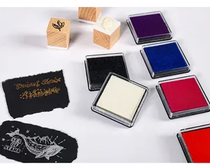 Detalle de almohadillas de tinta de colores con sellos metálicos en papel negro.