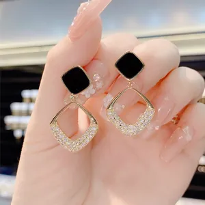 Detailed close-up shot of geometric black and gold pavé diamond drop earrings on hand