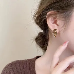 Nahaufnahme der eleganten, minimalistischen, blattförmigen Goldohrringe am Ohr eines Models