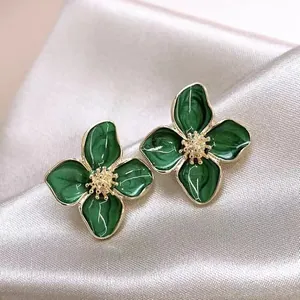 Primo piano di eleganti orecchini a lobo a fiore in smalto verde con bordi dorati