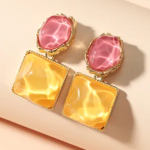 Dettaglio ravvicinato di orecchini geometrici con texture a onde rosa e gialla.