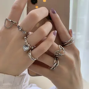 Detailed close-up of silver heart and chain rings on fingers holding a smartphone