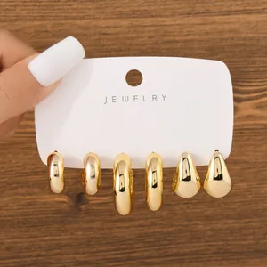 Set of three pairs of chunky gold hoop and teardrop earrings on a white display card