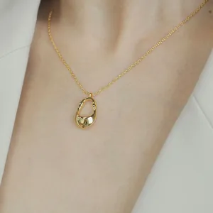 Primo piano di una collana con pendente dorato irregolare minimalista indossata da una modella
