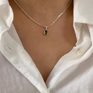 Close-up view of a green agate teardrop pendant silver necklace worn over a white shirt.