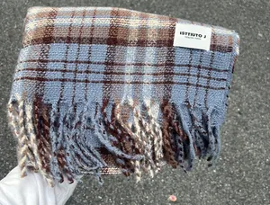 Close-up detail shot of a soft blue and brown plaid scarf with tassels and brand tag