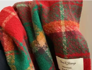 Close-up of red and green plaid Christmas scarf showing texture and brand label.