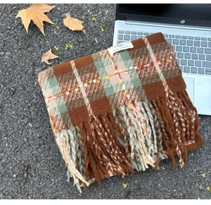 Macro view of brown and green plaid scarf with fringes on autumn leaves background
