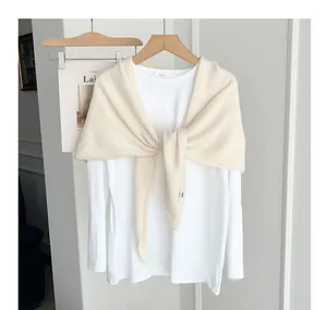 Detail of a soft cream knitted shawl draped over a minimalist white shirt.
