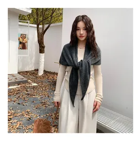 Elegant dark grey knitted triangular shawl scarf worn over a cream ribbed sweater.