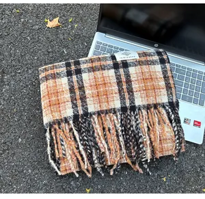 Detailed macro view of a warm orange and black plaid cashmere-like scarf with tassels