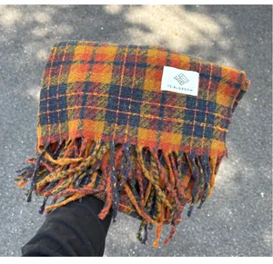 Close-up detail of a thick cashmere-like plaid scarf featuring tassels and white label