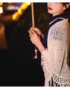 Detailed view of an elegant white hollow-out knitted shawl with fringe over a dark qipao.