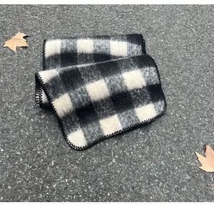 Close-up of black and white plaid mohair scarf with stitched edges on asphalt