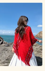 Red ethnic style knitted poncho with colorful trim and fringe in a scenic outdoor setting