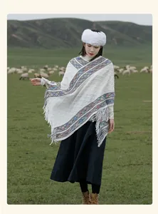 Ethnic white knitted winter poncho with colorful diamond patterns and tassels worn outdoors