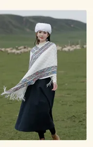 Ethnic style knit poncho with colorful tassels worn by a model in a scenic meadow