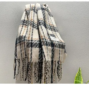 Close-up detail view of a thick plaid winter scarf featuring long fringes and a sewn label