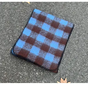 Close-up detail of a blue and brown checkered mohair scarf with stitched edges on asphalt