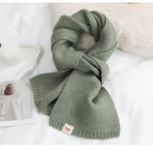 Detailopname van een zachte saliegroene gebreide sjaal met een minimalistisch textiellabel.