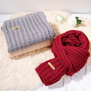 Sciarpe invernali in lana a maglia grigie, crema e rosse su un morbido tappeto bianco
