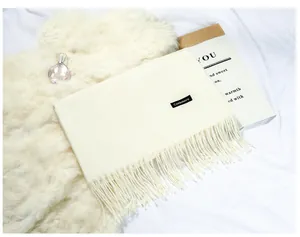 Close-up of a soft cream faux cashmere scarf featuring elegant fringe and a black label