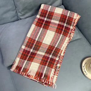Vintage red plaid winter scarf for women with fringe on grey sofa background